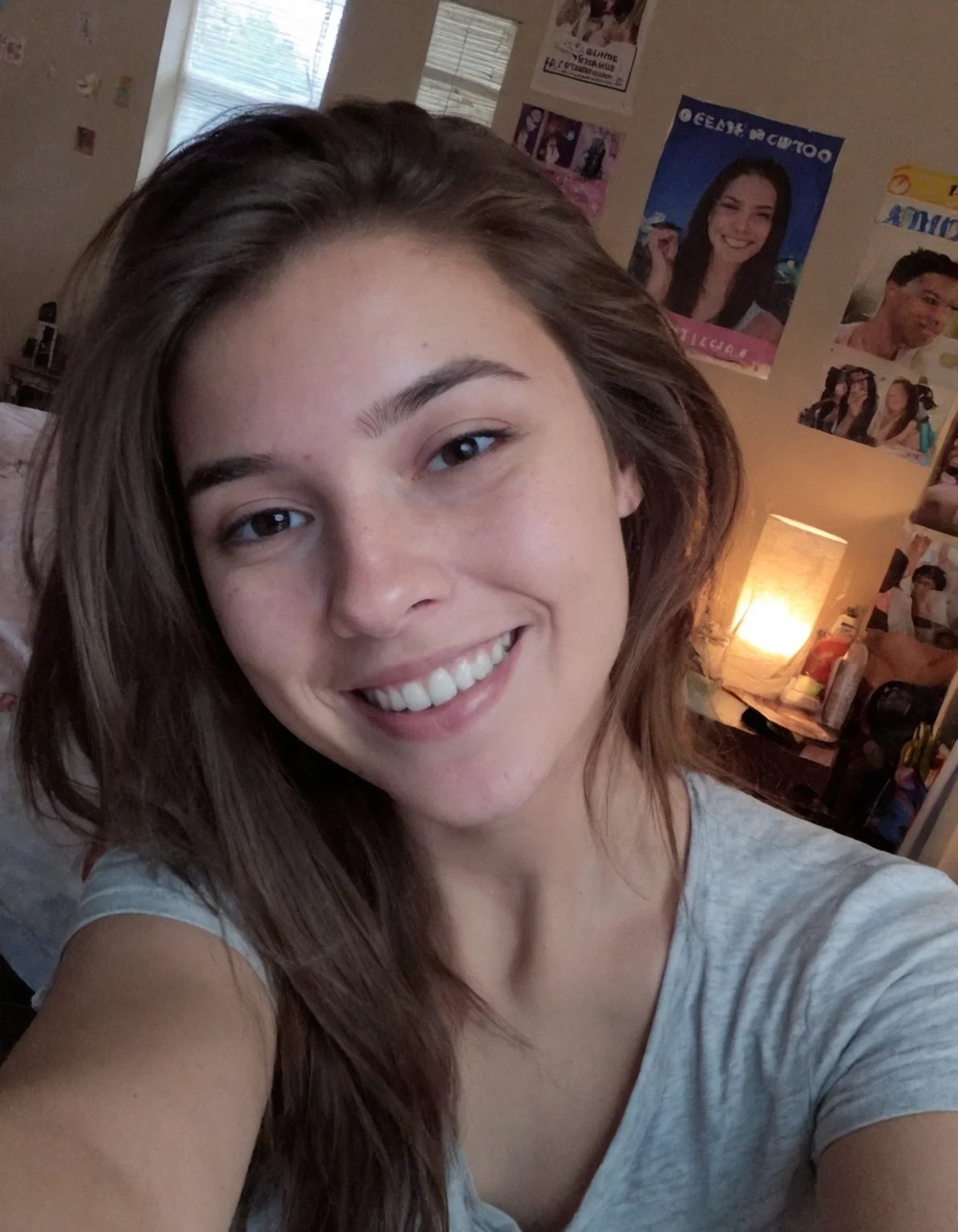 Authentic share, Amateur quality phone photo, A young woman taking a selfie with her phone, typical of a 2015 Snapchat post. She is smiling casually, with minimal makeup, in a casual setting like her bedroom. The lighting is soft and natural, coming from a window, and the background shows some personal items like posters and a bed
