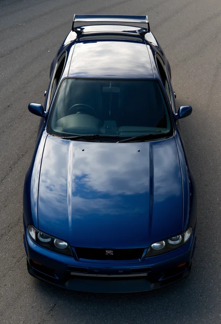 <lora:Nissan_Skyline_GT-R_R33:0.8> A slightly from above of a modified Nissan Skyline GT-R R33 in all its shining glory. Mirror-like, glossy finish.