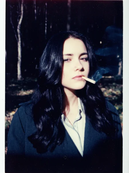 p0l2rd, Young woman, early 20s, casual style, wearing dark trench coat and white office shirt, long wavy black hair cascading over her shoulders, slightly parted lips with lit cigarette with smoke between them, looking direct at the viewer, makeup, sad and tired expression, standing outdoors in the dark forest, autumn, sunlight filtering through the trees. overexposed and blurry photo with blue and purple tones