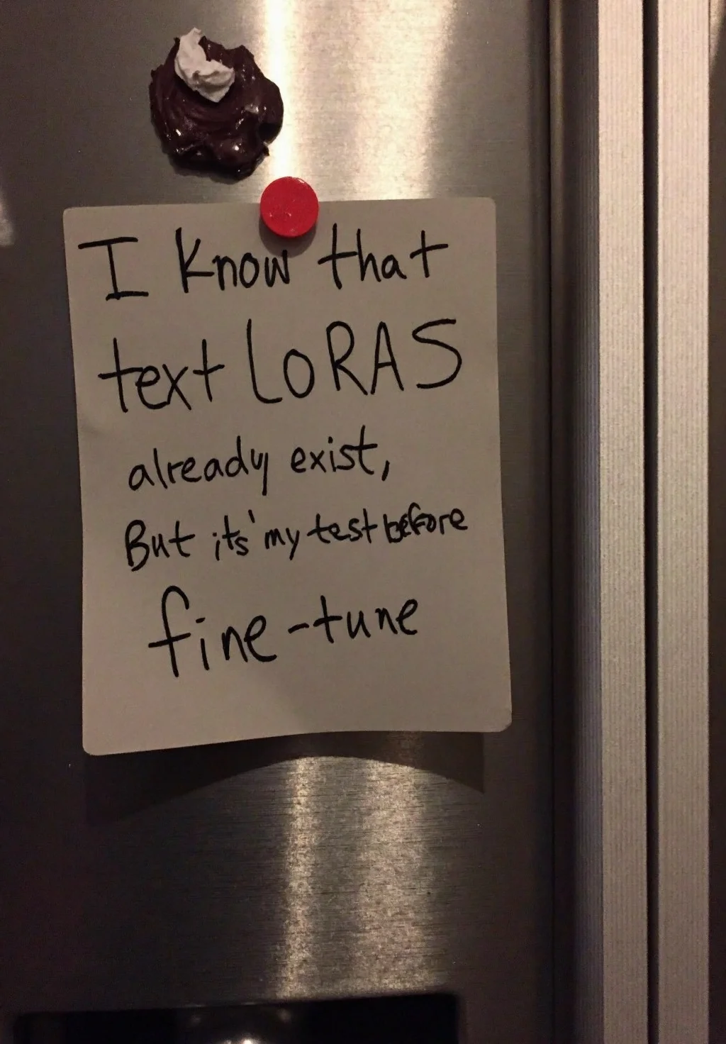 Fridge in modern kitchen, silver stainless steel finish, two-door design, freezer compartment on top, various magnets and notes attached, Handwritten note secured by red magnet on a slightly crumpled paper, text reads I know that text LoRAs already exist, but it's my test before new fine-tune, in black ink, uneven edges, paper appears grayish in color, simple handwritten style, text centrally aligned, close-up view, subtle shadows cast on fridge surface, slightly overexposed highlights on stainless steel texture, straight-on angle, indoor setting, artificial warm lighting.