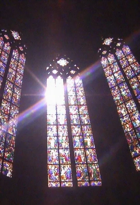 v8s, Vibrant stained glass window, multiple tall panels, intricate colorful designs, depicting various figures, indoors of a cathedral or church, dark surrounding interior, bright light streaming through, rainbow-like lens flare visible, overexposed lighting, daytime, upward angle view, strong contrast between illuminated glass and dim interior, no visible text or signage, detailed artwork, spiritual or religious theme, captured in a high-ceilinged space, ethereal atmosphere., . Amateur quality, Analog distortion, low resolution, Chromatic aberration, tape noise, Grainy texture, Frame jitter, muted colors, overexposed foreground