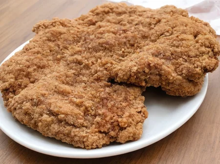 A high-resolution, hyper-realistic image of a deliciously fried chicken cutlet, referred to as G8G. The G8G is golden brown, with a crispy, crumbly coating and tender, juicy meat inside. It's served on a rustic wooden plate, with a side of fresh, colorful vegetables and a dollop of tangy sauce. The scene is set in a cozy, homely kitchen, with all elements in sharp focus, creating a clear and detailed image. The lighting should be warm and inviting, highlighting the appetizing qualities of the G8 and the cozy atmosphere of the setting, <lora:g8:0.7>