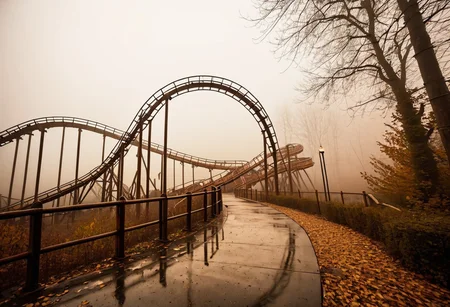 photo, abandoned theme park, theme park rides, fog, foggy, haze, low light, diffused light, very low saturation, dirty, creepy, spooky, natural looking photo, atmospheric, outside, autumn, roller coaster, extremely detailed, high quality,