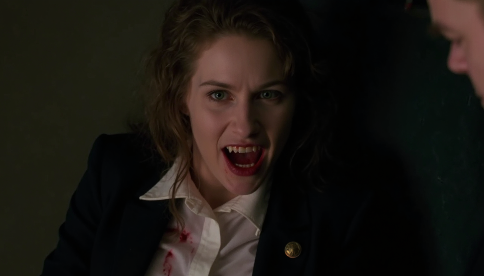 cinematic close-up shot of a young vampire business woman with fangs sitting on a desk, looking intensely at the viewer, very pale skin, mouth open showing fangs, blood around mouth, blood on white blouse, dark suit, messy hair hanging over face, lit from one side by a desk lamp with cold light, shadow on the other side, strong contrast between pale skin and blood, analogue film, IMAX, photorealistic, very detailed <lora:iwtv_flux_1_0:1>