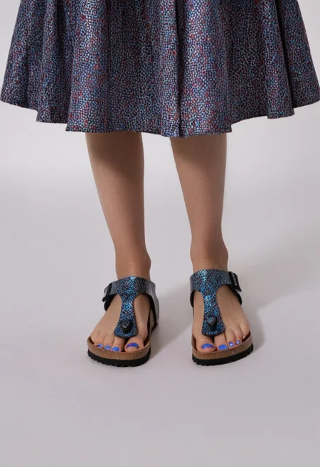 1girl, solo, dynamic_pose, simple_background, white_background, gizehonfeet, blue_toenail_polish, close-up, lower_body, footwear_focus, patterned, long_skirt