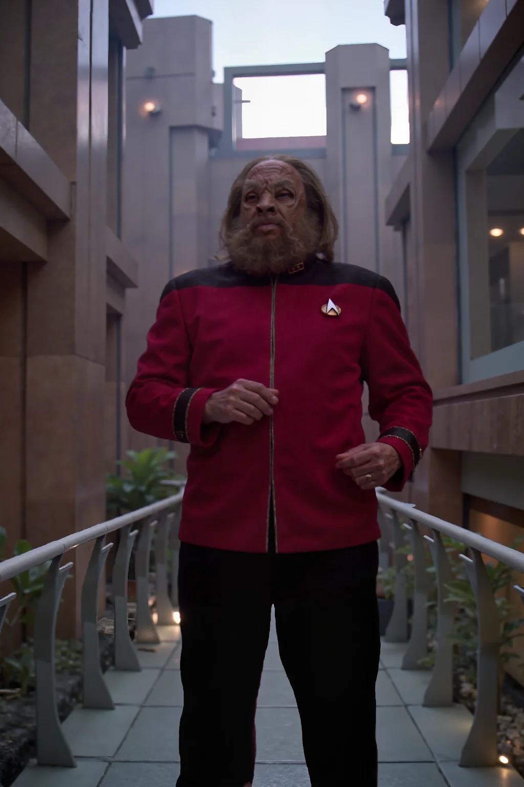 tellarite with a beard and long hair in maroon TNGadm jacket with black shoulders and black pants standing on a glass bridge connecting two scifi buildings , detailed background Fantastic lighting. Detailed shadows.intricate details, vivid colors, hyper-detailed, ultra-sharp <lora:ST_TNG_ADMIRAL_FLUX><lora:tellarite_FLUX>