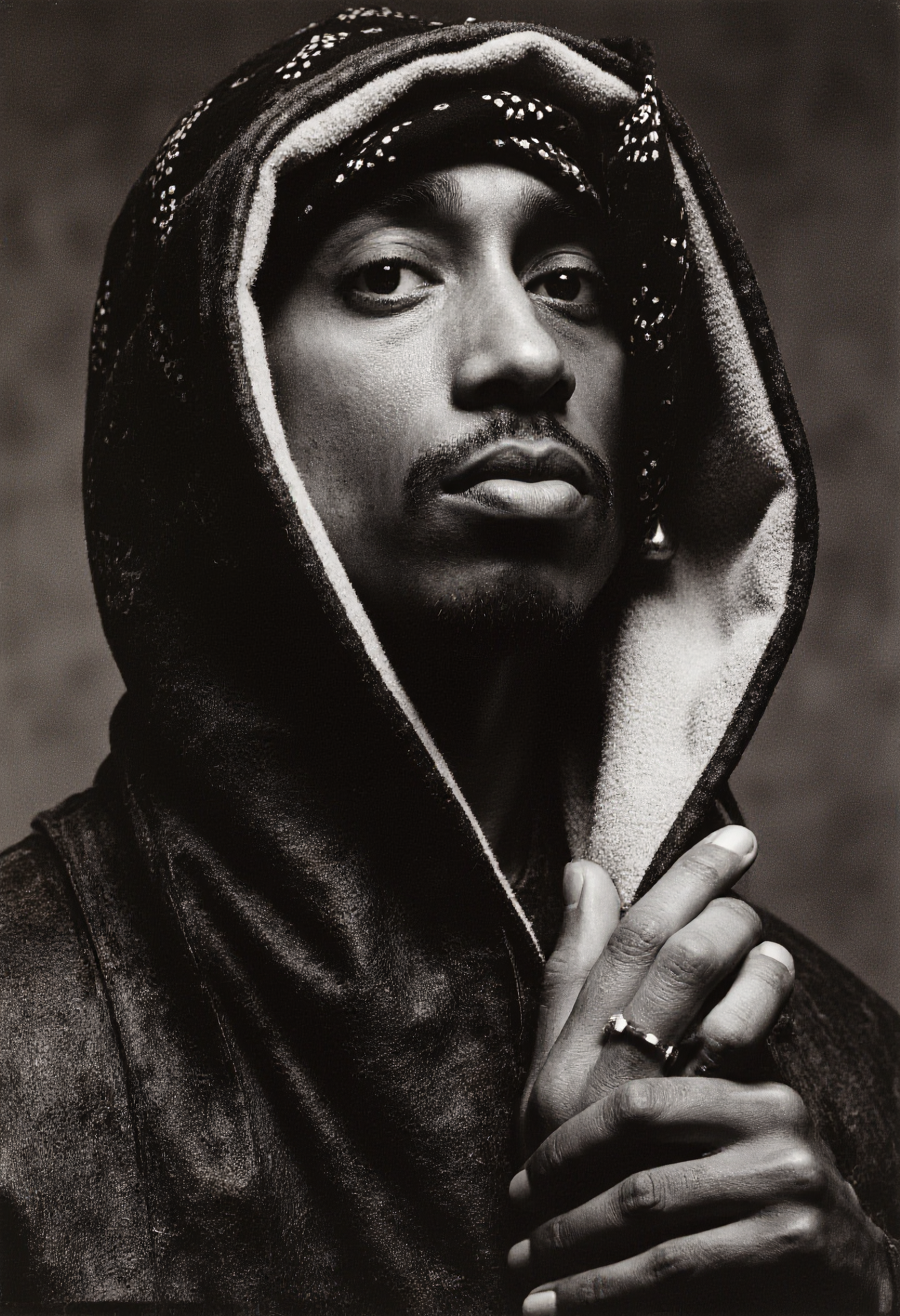 A high-contrast photo of a Tupac Shakur, captured as a black and white portrait, posing for a picture in the style of david-bailey. The subject is centered and gazing directly at the camera, showcasing his expressive eyes and a confident yet thoughtful demeanor. His iconic bandana and minimalistic jewelry enhance the timeless appeal of the image. The background is softly blurred to emphasize the subject, with subtle hints of a gritty urban setting. The lighting accentuates sharp contrasts and detailed textures, creating dramatic shadows that highlight his features. This image is taken with a classic Leica M6 camera, using a standard 50mm lens, capturing the depth and tonal range characteristic of high-end analog photography. <lora:david-bailey-flux1-dev-v1:1>