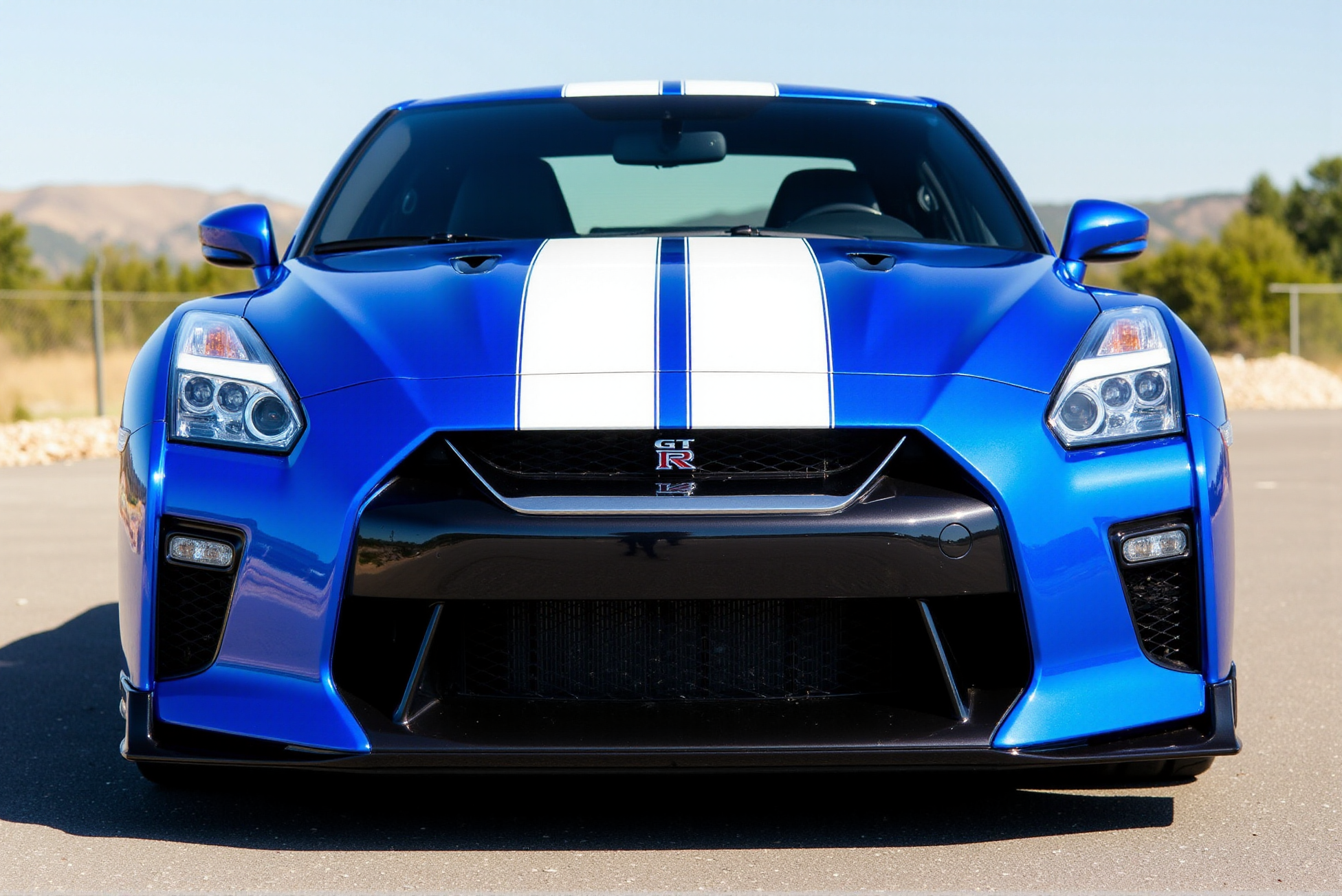 <lora:Nissan_GT-R_R35:0.8> 
A deep metallic blue Nissan GT-R R35 rests calmly under a softly clouded sky, captured in warm golden-hour lighting on a gravel-covered open lot. The low-slung stance, sharply sculpted hood, and flared front wheel arches convey poised aggression, while the sleek aerodynamic body panels reflect the muted amber light. The front grille prominently features the GT-R emblem set just above the chrome Nissan badge, both gleaming with subtle intensity. Multi-spoke alloy wheels finished in brushed silver house ventilated brake rotors and red Brembo calipers stamped with white branding. The side mirrors and front splitter echo dark gloss finishes, and the slight tilt in the camera angle adds a cinematic tension. Faint reflections ripple across the body, and thin wisps of fencing in the distance add scale and openness to the composition. The contrast between the grounded solidity of the vehicle and the expansive background builds visual drama, emphasizing the GT-R R35âs balance of power and elegance. Subtle tire tread texture and shadow gradation beneath the chassis provide depth and tactile realism, enhancing the visual gravity of this iconic performance coupe in a still, contemplative moment.
