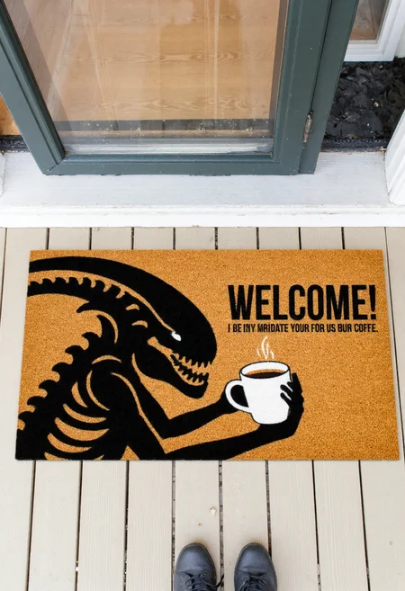 <lora:Welcome_Mat_Manufacturer_FLUX-000023:0.9>
The image is a photograph of a small outdoor entrance area, featuring a doormat with a humorous design. The doormat is rectangular and made of a textured, brown, coir material. It has a vibrant, whimsical design featuring a black xenomorph holding a cup of coffee and text "WELCOME!"