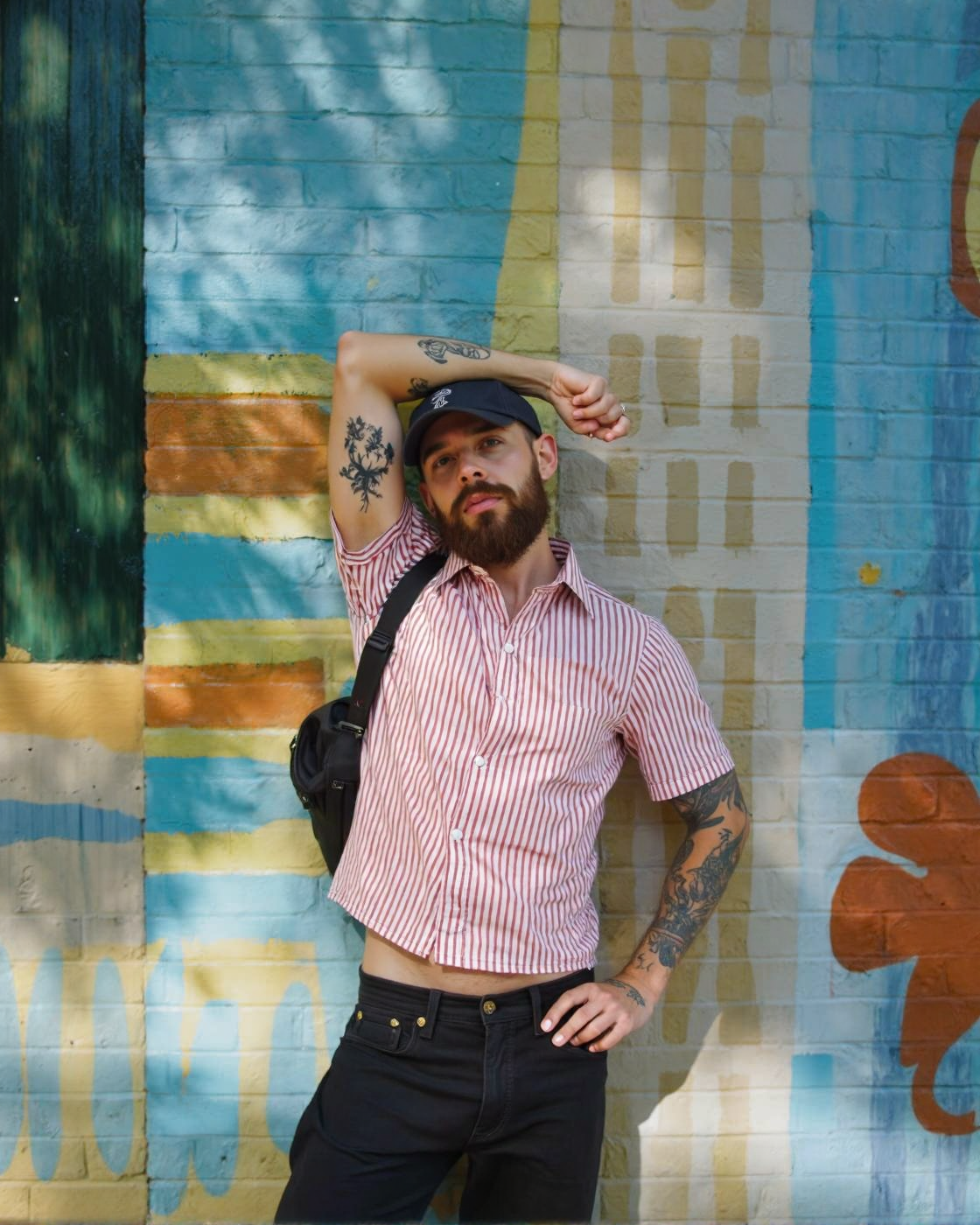A man with a beard and tattoos standing in front of a colorful striped wall, posing confidently with one hand on his hip and the other resting on his thigh. he is wearing a red and white striped button-up shirt, black pants, and a black bag slung over his shoulder. his body is slim, and he has a beard. he has several tattoos on his arms, including one on his left arm and another on his right arm. he also has a cap on his head and a ring on his finger. the man is looking directly at the camera with a serious expression. the background is a vibrant outdoor setting with a striped wall in shades of blue, green, and yellow.
ðï¸ [Inpainted with Loras]: flux1-depth-dev-lora
ð¯<lora:flux\loratools\flux1-depth-dev-lora.safetensors:0.75:0.75>