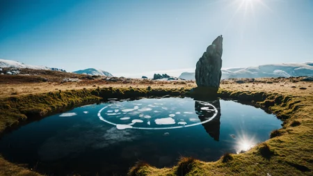 A cinematic scenic photography of the view On a hidden mountain tarn beneath an ancient stone circle. At winter midday, bright sun reflects on crystalline ice, crisp shadows etch every monolith, and swirling vapor drifts from hidden crevasses. ,, masterpiece, best quality, amazing quality, very aesthetic, high resolution, ultra-detailed, absurdres, scenery, film grain, HDR, 8K, high contrast, realistic, cosplay, muted lithing, sharp focus, (chromatic aberration), fine details,