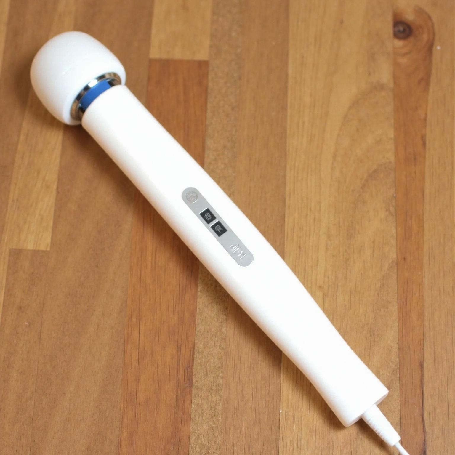 A photograph of a white wand vibrator a round white head and a silver button on the side. The vibrator is placed on a wooden table.   <lora:WandVibratorV1FLUXD:1>