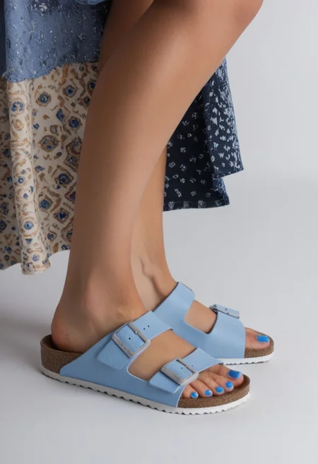 1girl, solo, simple_background, white_background, birksonfeet, blue_toenail_polish, close-up, lower_body, footwear_focus, patterned, long_skirt