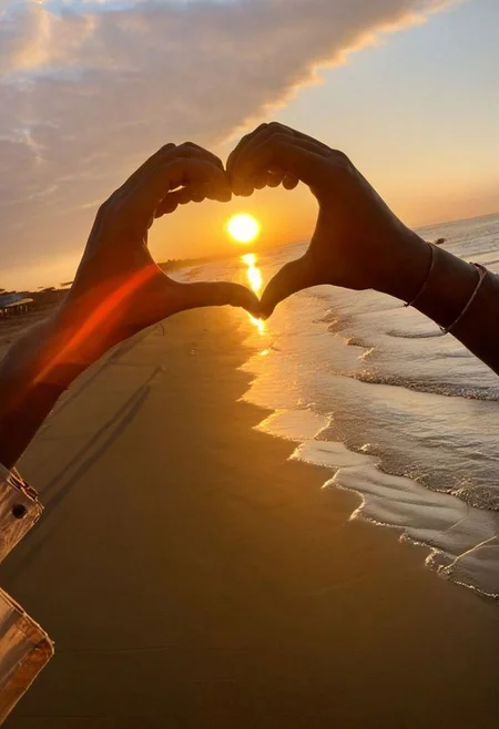 F-B-C, POV, foreground: two hands in the shape of a heart  , background: sunset on the beach , effect: the sun is on the center of the heart