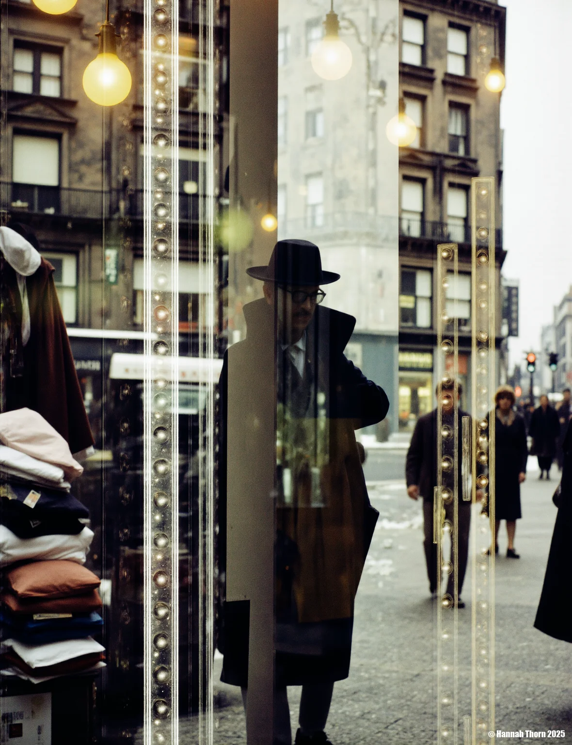 The picture is a photograph that appears to be taken through a shop window. **Description:** The main focus is a blurry, partially obscured figure of a person wearing a fedora hat, positioned centrally. This figure is reflected in a glass surface, which creates a double image effect. The reflection is superimposed over a street scene visible through the shop window. The street scene shows piles of stacked merchandise, possibly clothing, with price tags or signs visible. There's also a building in the background with architectural details suggestive of an older style of building. Several light bulbs are visible both inside the shop and reflected on the street outside. The overall atmosphere is one of urban life, possibly in a city during a cold season. Other blurry figures of people can be seen moving in the street scene. The details of the street scene are not entirely clear due to the reflection and blur. **Style:** The style of the photograph is reminiscent of street photography, with a focus on capturing candid moments of urban life. The use of reflections and blurring adds an element of abstraction and mystery. It exhibits the characteristics of a slightly surreal, dreamlike quality due to the way the reflection interacts with the scene. The overall aesthetic is gritty, evocative of a certain era. The monochrome palette enhances this effect, emphasizing the contrasts in light and shadow. The photographer seems to be interested in exploring the intersection of the interior and exterior spaces through the medium of reflection. The style aligns with a modernist approach to photography, valuing observing and recording moments of contemporary life in an unconventional way. There's a strong contrast between the sharpness of some elements (like the building) and the intentional blurriness of others (the people and the central figure), creating a layered depth and visual interest. <lora:_Flux\Saul_Leiter_Streetphotography.safetensors:1.0:1.0>