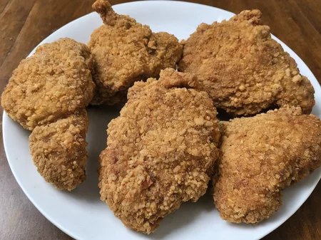 A high-resolution, hyper-realistic image of a deliciously fried chicken cutlet, referred to as G8G. The G8G is golden brown, with a crispy, crumbly coating and tender, juicy meat inside. It's served on a rustic wooden plate, with a side of fresh, colorful vegetables and a dollop of tangy sauce. The scene is set in a cozy, homely kitchen, with all elements in sharp focus, creating a clear and detailed image. The lighting should be warm and inviting, highlighting the appetizing qualities of the G8 and the cozy atmosphere of the setting, <lora:g8:0.7>