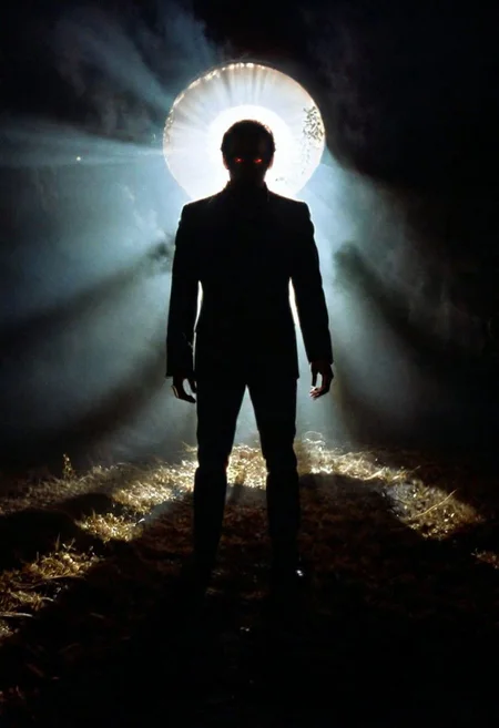 A shadowy silhouette with glowing eyes is standing in a dark room. The darkness of the room and the man's eyes create a striking contrast, drawing attention to the subject. The man is the main focus of the image, and his presence in the dark room adds an element of mystery and intrigue. 1970s horror film