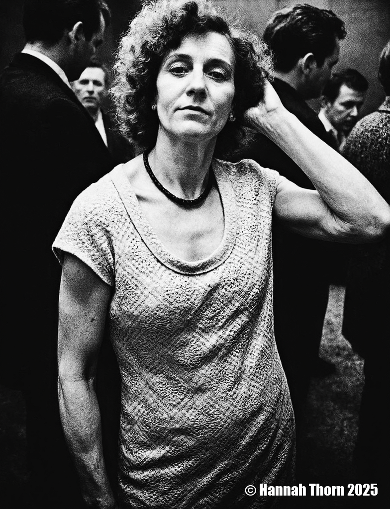 A black and white photograph from a portrait camera angle about a middle-aged woman with curly hair, wearing a knitted dress, standing in a dimly lit room with blurred figures in the background. the woman, who appears to be in her late 60s or early 70s, is standing in the middle of the image, with her upper body facing the viewer and looking directly at them. she has a serious expression and is wearing a sleeveless, lace-like dress with a black beaded necklace around her neck. her curly hair is styled in a way that frames her face and adds to her natural beauty. the background is out of focus, focusing attention on the woman and her outfit.<lora:_Flux\Anders_Petersen.safetensors:0.9:0.9>