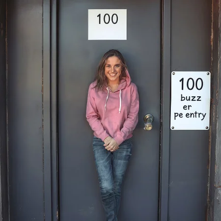 a locked door with a white sign that reads "100 buzz per entry". Outside the door there is a woman 26 years old model. Very clearly desperate to pee. Wearing jeans. Wearing pink hoodie. Squeezing legs together tightly. Crossed legs. Very desperate to pee. Door is closed. She is looking at viewer. She is smiling. She really need to pee.