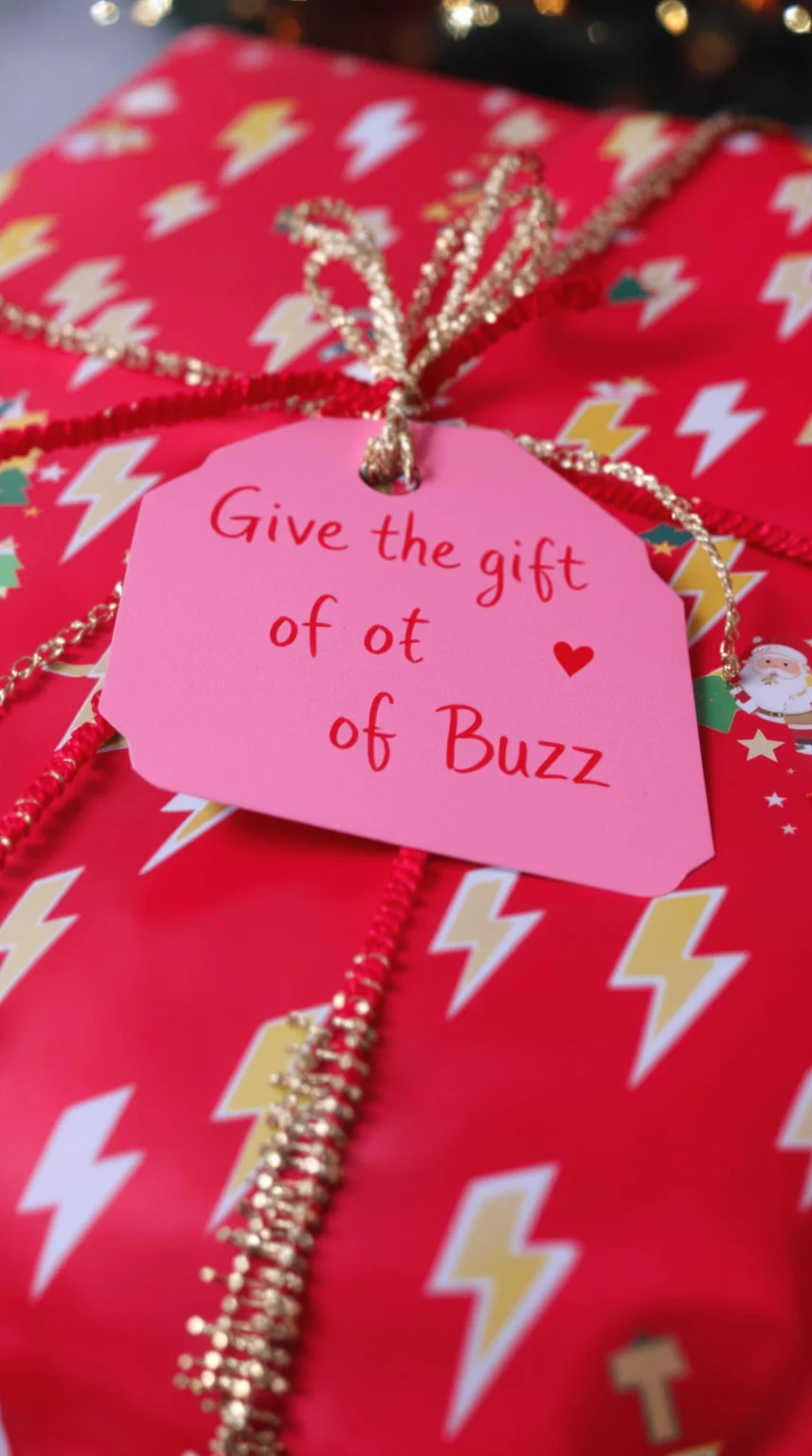 comical close-up of a Christmas present with lightning bolt symbols on the wrapping paper, with a gift tag that has the words "Give the gift of Buzz" written in a cursive christmas font.