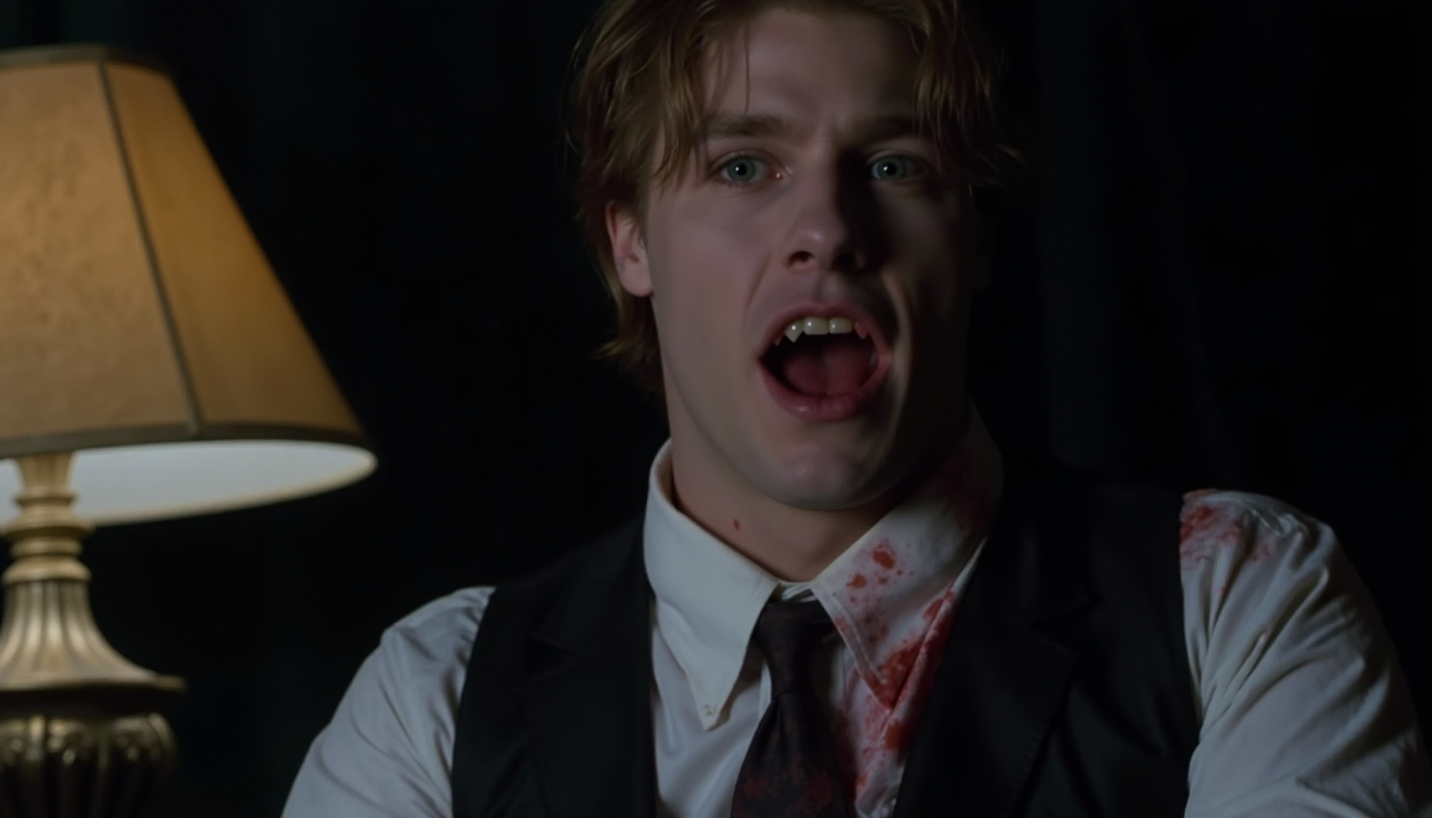 cinematic close-up shot of a young vampire business man with fangs sitting on a desk, looking intensely at the viewer, very pale skin, mouth open showing fangs, blood around mouth, blood on white shirt, loosened tie, dark suit, messy hair hanging over face, lit from one side by a desk lamp with cold light, shadow on the other side, strong contrast between pale skin and blood, analogue film, IMAX, photorealistic, very detailed <lora:iwtv_flux_1_0:1>