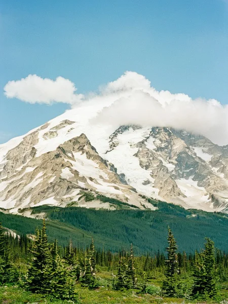 film photography style a snowy mountain range with a forest in the foreground, fluffy clouds in the sky, early morning <lora:FILM_PHOTOGRAPHY_STYLE-000017:1>