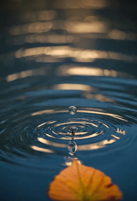 A macro photograph captures the precise moment a water droplet hovers above a golden autumn leaf floating on a dark blue water surface. a low angle shot of leaf with bokeh effect, realistic reflection over water, The leaf displays intricate venation patterns and rich orange coloration, while the perfectly formed water droplet exhibits crystal-clear transparency and light refraction. The scene is illuminated by artificial backlighting that creates dramatic contrast between the warm-toned leaf and the cool blue water background. Circular ripples in the water surface and subtle bokeh effects add depth and atmosphere to the composition. Macro photography with artificial backlighting and shallow depth of field creates sharp focus on the subject against a blurred background.
