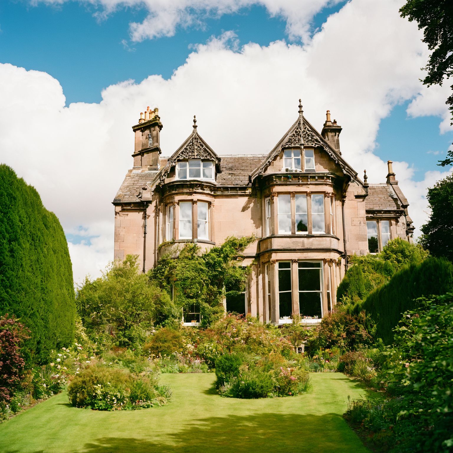 film photography style a victorian house in Scottland, trees, fluffy clouds in the sky <lora:FILM_PHOTOGRAPHY_STYLE-000017:1>