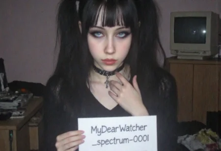 v8s, Young woman, early 20s, slim build, light skin, dark straight hair styled in pigtails, blunt bangs covering forehead, wearing black choker and black cross necklace, intense expression, front view, looking directly at the viewer, right hand near neck, left hand holding a sign with handwritten text "MyDearWatcher_spectrum_0001", dressed in casual dark-toned clothes, standing indoors in a low-lit room, background showing cluttered furniture, desk with retro computer and crt monitor, muted and desaturated colors