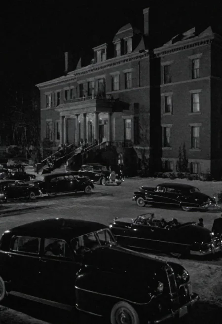In the 1950s in Chicago, outside at night, from afar you can see a luxurious mansion of the mafia boss, you can see several cars and many armed gangsters protecting. Captured with a 35 mm camera, black and white, classic film noir film.