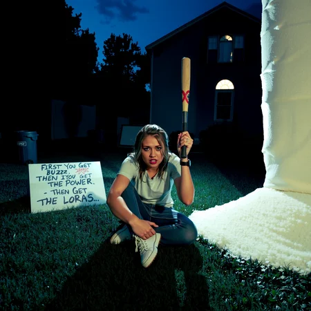A grainy candid surreal, cinematic scene at night, in the backyard of a suburban home. A realistic woman sits cross-legged on the blue grass, clutching a baseball bat in both hands with a wide-eyed, tense expression. She is in front of a massive, comically large pile of sugar standing as tall as the house. The woman has disheveled hair, casual clothes like a white t-shirt and jeans, and her posture is tense and alert, like she’s been sitting guard for hours. The lighting is dramatic and slightly off-kilter, with a blue-toned night sky and shadows stretching across the surreal suburban setting. Behind her is a trash can and a house with cracked windows. The entire scene has an eerie, hyperreal quality with an intentional touch of absurdity, like a realistic reimagining of a moment from a bizarre cartoon. Cinematic lighting, full-body composition, photoreal detail, next to the sugar there is a sign that reads "FIRST YOU GET THE BUZZ, THEN YOU GET THE POWER, THEN YOU GET THE LORAS"