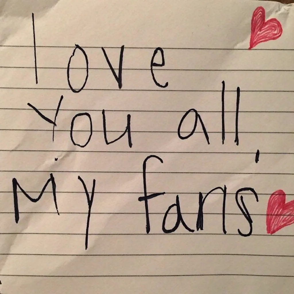 Crumpled piece of lined paper, handwritten message reading "love you all, my fans", written in black ink, neat and legible handwriting, paper background shows visible creases and shadows, natural indoor lighting, close-up angle, focus on text, warm tone lighting, small red hearts interspersed