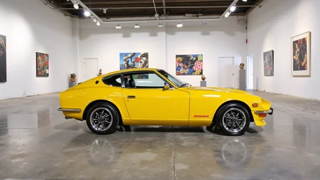 Inside a spacious, minimalist modern art museum with white walls and polished concrete floors, a 1972 Nissan Datsun 240Z Fairlady in radiant sunflower yellow stands as an exhibit. Overhead spotlights highlight the carâs long hood, round headlights, and chrome-accented mirrors. Abstract sculptures and large colorful canvases surround the car, creating a striking juxtaposition between classic automotive beauty and contemporary artistic expression
<lora:ral-nssndtsn_000001000:1>