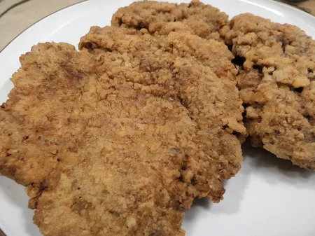 A high-resolution, hyper-realistic image of a deliciously fried chicken cutlet, referred to as G8G. The G8G is golden brown, with a crispy, crumbly coating and tender, juicy meat inside. It's served on a rustic wooden plate, with a side of fresh, colorful vegetables and a dollop of tangy sauce. The scene is set in a cozy, homely kitchen, with all elements in sharp focus, creating a clear and detailed image. The lighting should be warm and inviting, highlighting the appetizing qualities of the G8 and the cozy atmosphere of the setting, <lora:g8:0.7>