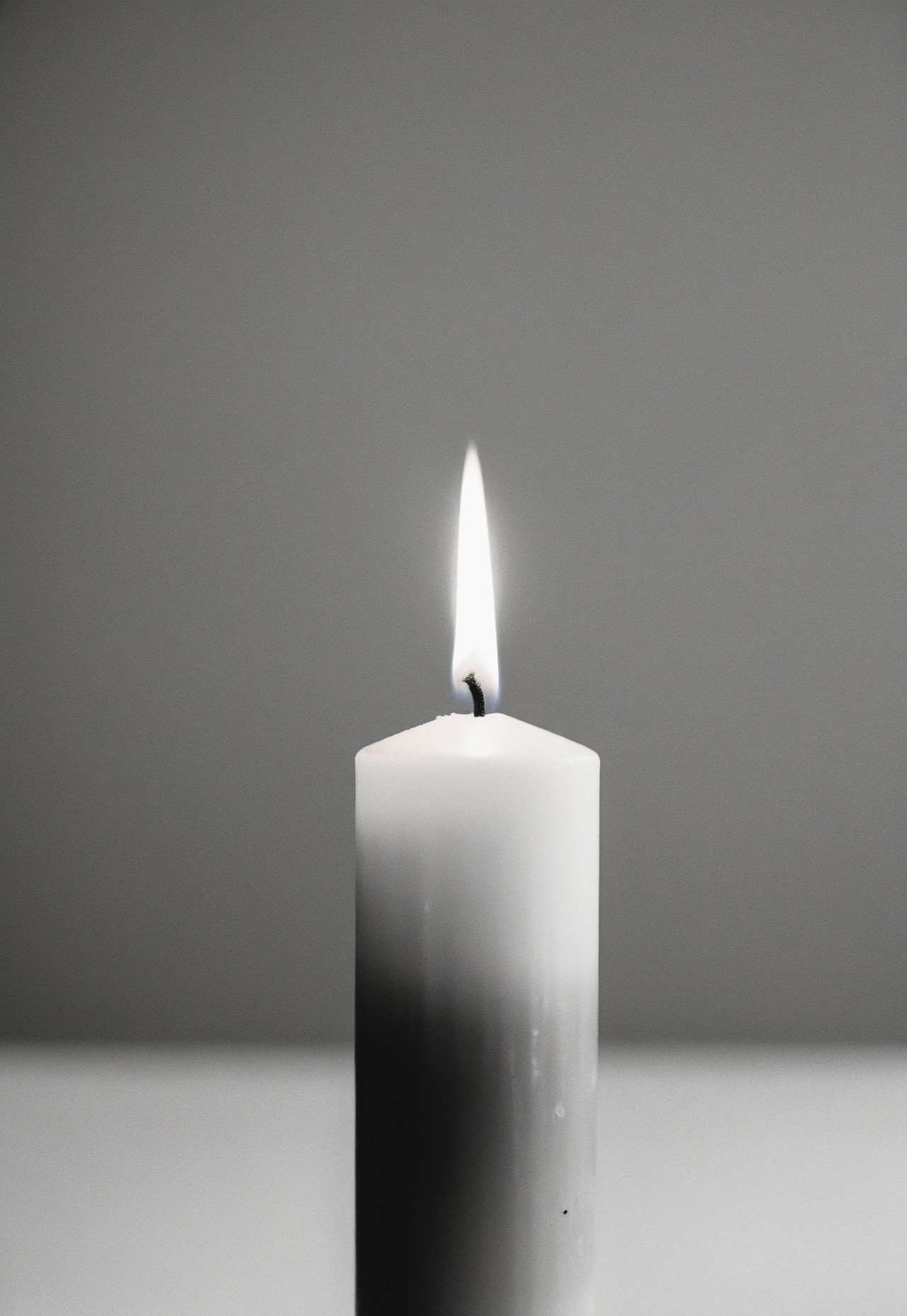 Close up of a Unique Looking Candle in the middle on a Black Table, Completely white background, Soft diffused lighting, grayscale, Monochromatic, Muted Tones, Minimalist, Ethereal, Leica MP, Leica Noctilux 50mm f0.95  Lens, Kodak Tri-X 400 Film, 35mm Film, Film Grain, Film halation