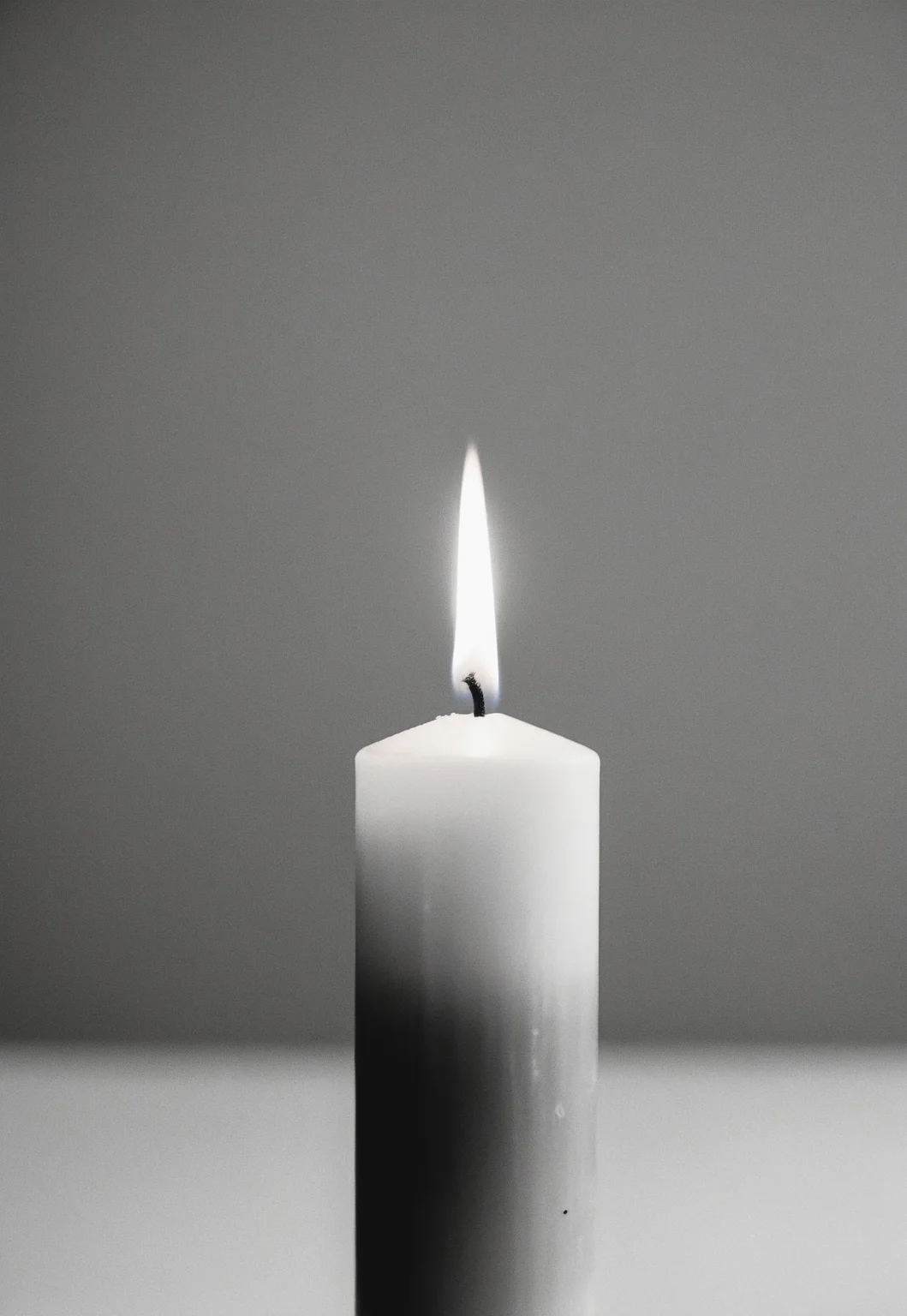 Close up of a Unique Looking Candle in the middle on a Black Table, Completely white background, Soft diffused lighting, grayscale, Monochromatic, Muted Tones, Minimalist, Ethereal, Leica MP, Leica Noctilux 50mm f0.95 Lens, Kodak Tri-X 400 Film, 35mm Film, Film Grain, Film halation