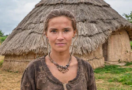 photograph,a beautiful neolithic woman in front of a neolithic hut, background a neolithic village,  high quality photography, 4k, Canon EOS R3, hdr, smooth, sharp focus, high resolution, award winning photo,