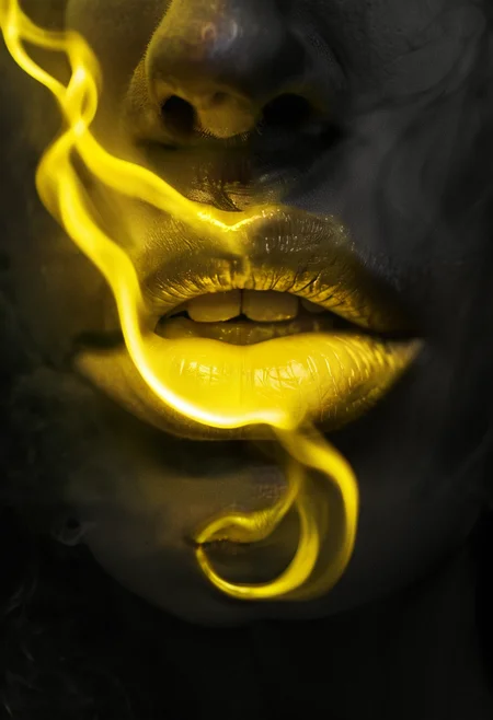 A close-up photograph of a woman's lips in monochrome, except for her lips, which are a vibrant, glowing yellow. Soft, ethereal yellow smoke-like waves emanate from her lips, flowing gently into the surrounding air. The rest of the image remains in black and white, creating a stark contrast with the vivid yellow glow, emphasizing the surreal and dreamlike quality of the scene