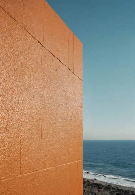Vintage film photography aesthetic, close up of A orange Wall Covering a half of the photo while the other half a breathtaking sea, Clear sky, natural light, Afternoon, Nikon F3, NIKON NIKKOR 24MM F/2.8 AIS LENS, F/4, ISO 100, agfa vista 400 Film, 35mm film, halation, Colour Density, Film Grain