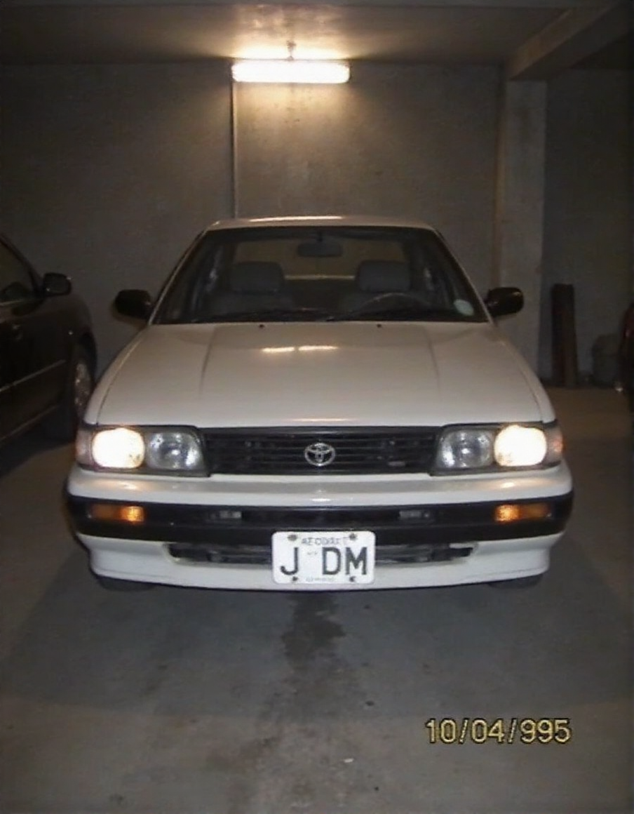 Toyota AE86, dusty, garaged, dim light from lamp above, headlights fogged up from wear, photo of front of car, license plate "JDM", date bottom right "10 04 1995",  <lora:2000analogcore_v3:1.5>