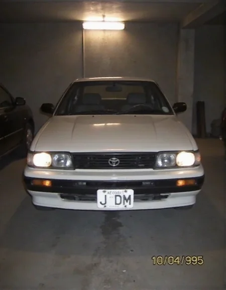 Toyota AE86, dusty, garaged, dim light from lamp above, headlights fogged up from wear, photo of front of car, license plate "JDM", date bottom right "10 04 1995", <lora:2000analogcore_v3:1.5>