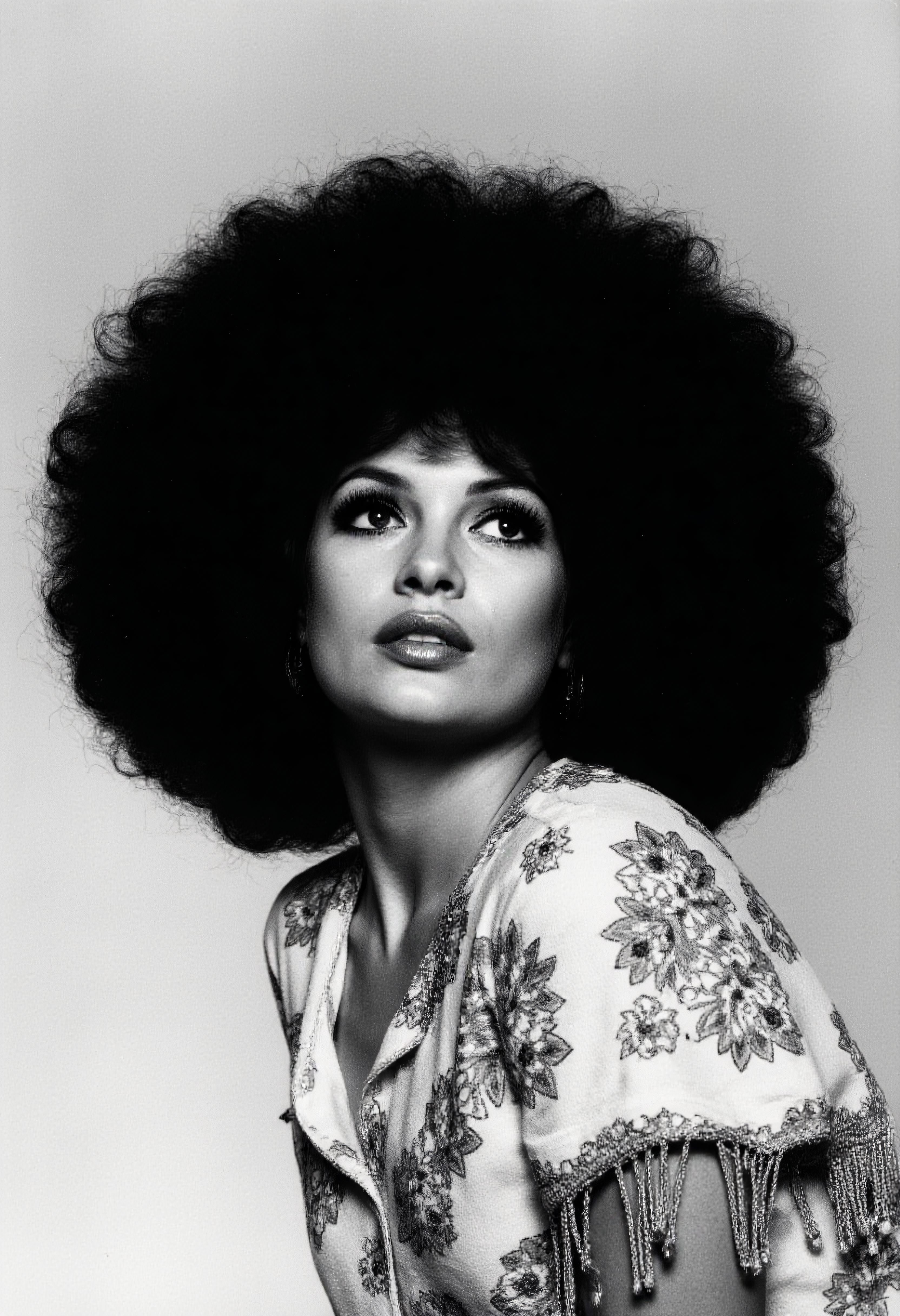 A high-contrast photo of a glamorous woman with a voluminous afro hairstyle, captured in a striking black and white portrait. She is elegantly posing for a picture, her expressive eyes adorned with dramatic eyelashes, gazing upward with confidence and grace. The composition includes intricate floral embroidery and fringed details on her draped outfit, evoking a 1960s aesthetic. The lighting accentuates her radiant features, and the style is heavily inspired by the iconic photography of david-bailey, emphasizing bold contrasts and timeless elegance. <lora:david-bailey-flux1-dev-v1:1>