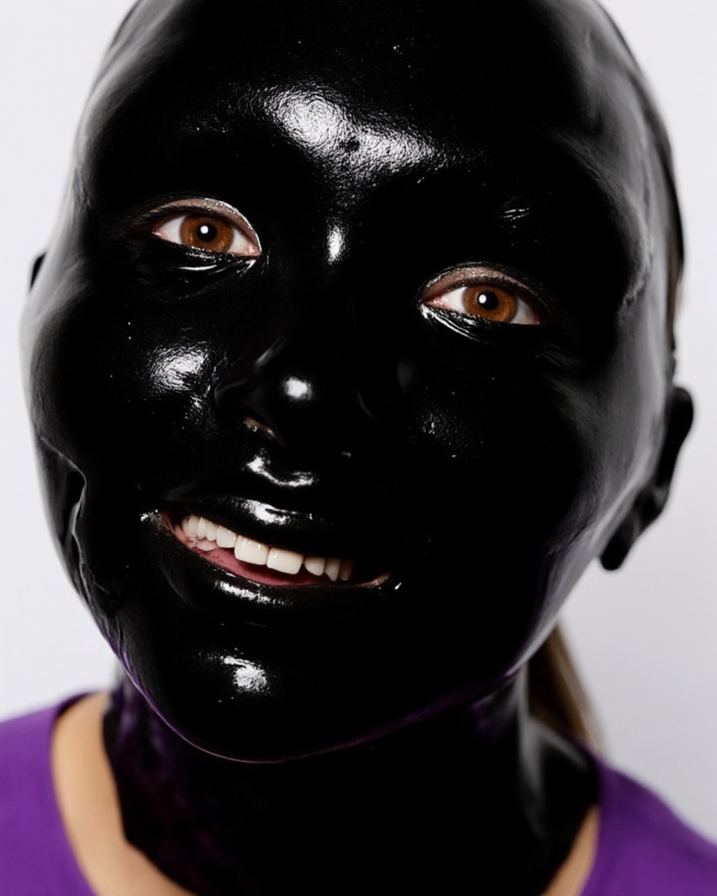 Kaos, This is a high-resolution photograph featuring a person's face covered entirely in a shiny, black, latex-like material. The material is stretched tightly over the face, creating a glossy, reflective surface that captures and distorts the facial features. The person's eyes, nose, mouth, and other facial details are barely discernible through the material, which appears to be a latex mask or a very tight, shiny wrap. The texture of the material is smooth and reflective, with a slight sheen that catches the light, creating a glossy, almost wet appearance. The person's lips are visible, slightly parted, revealing a few teeth. They are wearing a purple shirt, visible at the neck, which contrasts starkly with the black material covering their face.