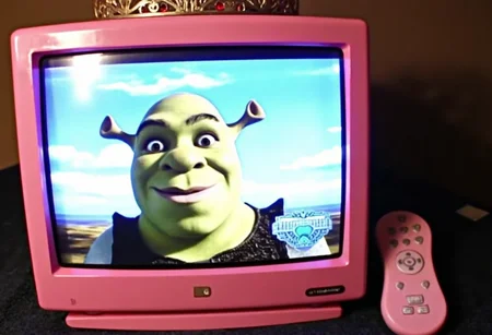aesthetic2000s, pink TV, vintage TV, princess TV, tiara, retro electronics, classic MTV, pop music, music video, shrek on screen, childhood nostalgia, pink remote control, gold tiara, red jewels, 90s style, early 2000s, cute design, entertainment, television screen, home decor, cozy room background, amateur photo