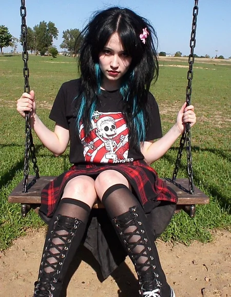 m8vic2, young woman with a pale complexion, wearing a gothic-inspired outfit. She has long, black hair with streaks of blue, styled in a voluminous, messy manner. Her hair is adorned with a small, pink bow on the left side. She is wearing a black t-shirt featuring a large, cartoonish graphic of a skeleton with red and white stripes, and a black and red plaid mini-skirt. Her legs are adorned with black, lace-up thigh-high socks, and she is wearing black and white canvas high-top sneakers. The socks have a prominent, criss-cross pattern, adding a punkish touch to her attire. She is sitting on a wooden swing set, holding onto the chains with both hands. The background shows an open field with green grass and scattered trees in the distance, under a clear, blue sky. The ground is a mix of dirt and grass, indicating a rural setting. The overall vibe of the image is edgy and rebellious, aligning with the gothic subculture