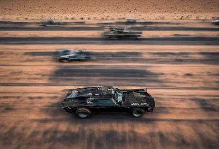 Creates an ultra detailed and realistic image taken by a drone, wide angle, of a race between 2 custom cars, created with parts from many muscle cars, with aerodynamic lines from 1972. The cars have tinted black windows. It is captured in motion with motion blur at full speed through a desert, daylight. Race between 2 cars. The photograph is captured with an Arri Alexa camera, with a zoom lens.
. <lora:Vintage Muscle Car SDXL:1>