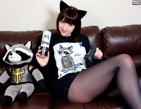 amateur photo of a 26 year woman with cat ears sitting on a sofa, gamer girl outfit and pantyhose, holding a "Colossus" energy drink and a ps5 controller, on her shirt is a cat cyborg comic with "Colossus" underneath it. the illustrated cat says "I am a Monster" . left to the woman is a raccoon plushie in knight outfit