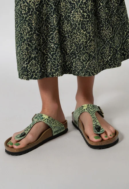 photograph of woman's feet wearing sandals, 1girl, solo, dynamic_pose, simple_background, white_background, gizehonfeet, (green toenail_polish), (close-up:0.5), lower_body, footwear_focus, patterned long_skirt