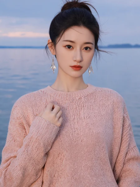 This photograph captures a young Asian woman standing by a serene, blue-hued lake with a distant, cloudy horizon. She is positioned slightly off-center to the right, adhering to the rule of thirds, creating a balanced composition. The woman has a slender physique, fair skin, and a delicate, refined face with subtle makeup. Her hair is styled in a casual bun with a few loose strands framing her face. She wears a light pink, textured knit sweater that adds a cozy, autumnal feel to the image. Her outfit is complemented by elegant, dangling silver earrings that catch the light, adding a touch of sophistication.
The background features a tranquil lake with gentle ripples, reflecting the soft, diffused light of either dawn or dusk, which casts a gentle glow on the scene. The sky is overcast, with a gradient of soft blues and grays, enhancing the calm and reflective mood of the image. The camera angle is at eye level, providing a clear, unobstructed view of the subject and the landscape. The overall lighting is natural and soft, with no harsh shadows, contributing to the serene and peaceful atmosphere.