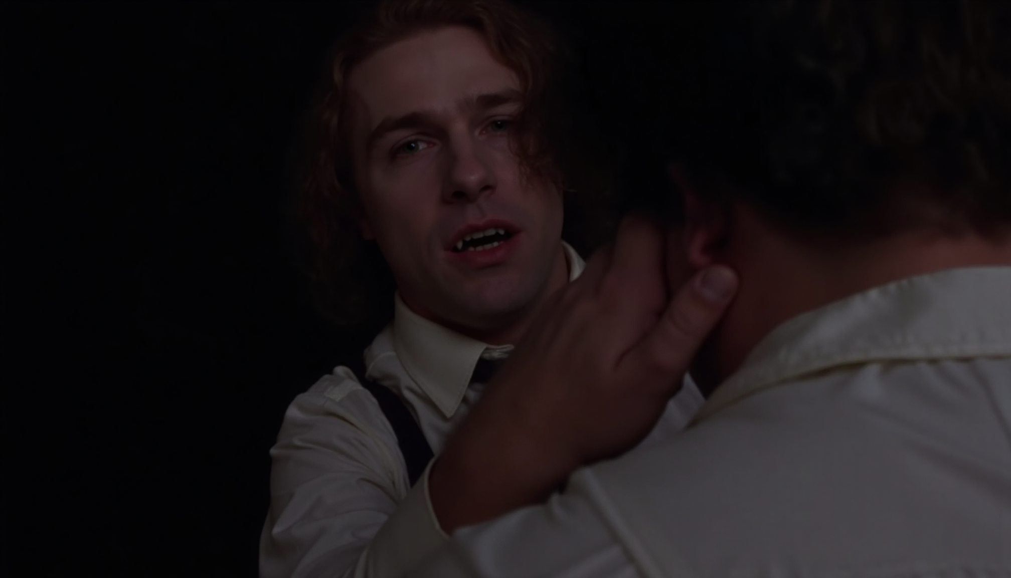 cinematic close-up shot of a vampire man with fangs and very pale skin shown looking over the shoulder of another man, preapring to bite, standing very close, one hand on the back of his neck. The other man is shown from behind, wearing a white shirt. At night in soft light. Analogue film, IMAX, photorealistic, very detailed <lora:iwtv_flux_1_0:1>